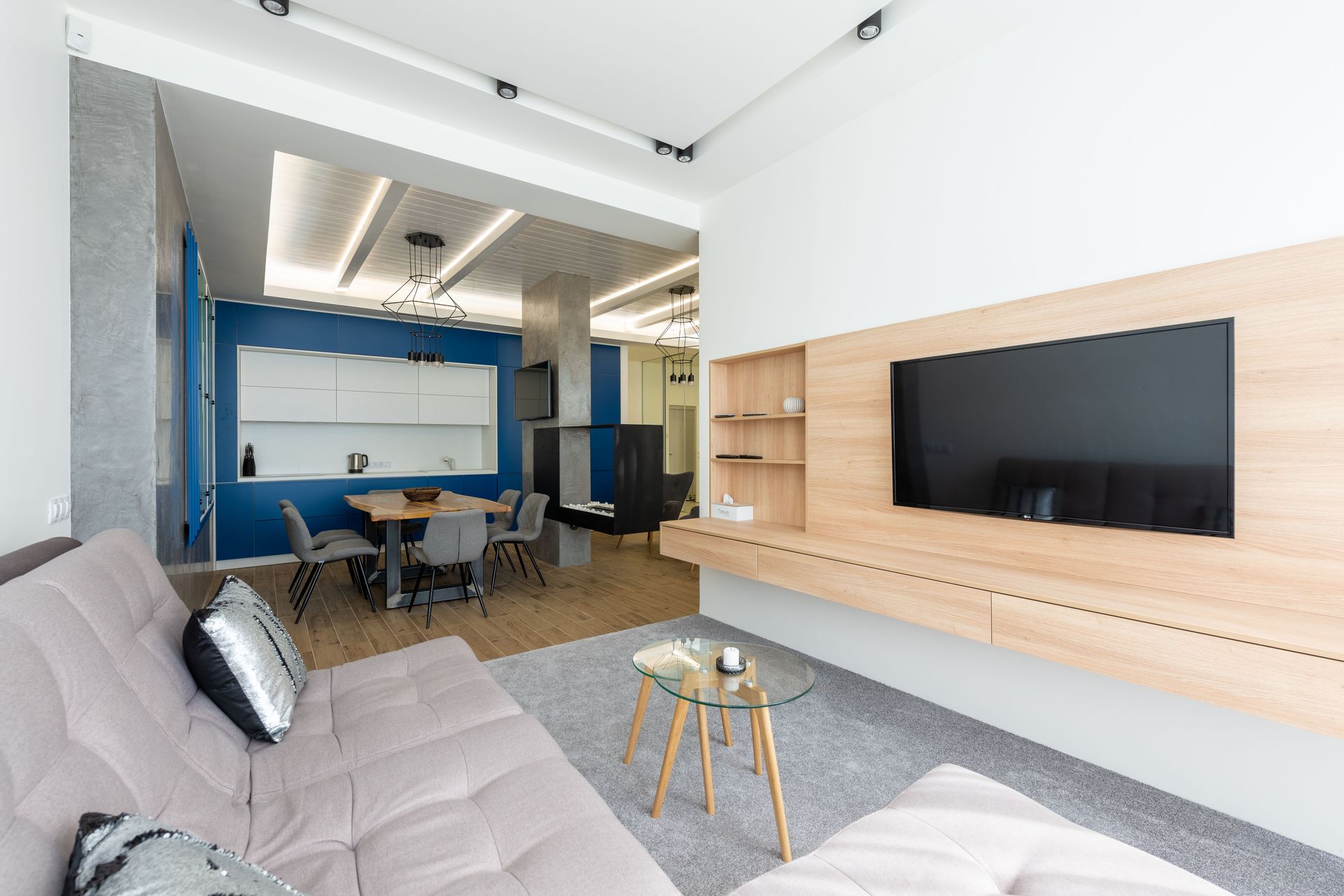 Interior of modern studio apartment with TV set hanging opposite sofa in living room and comfortable kitchen under luminous lights